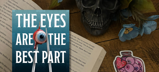 Picture of the book on a wooden backdrop with a back skull, and a little jar of eyeballs